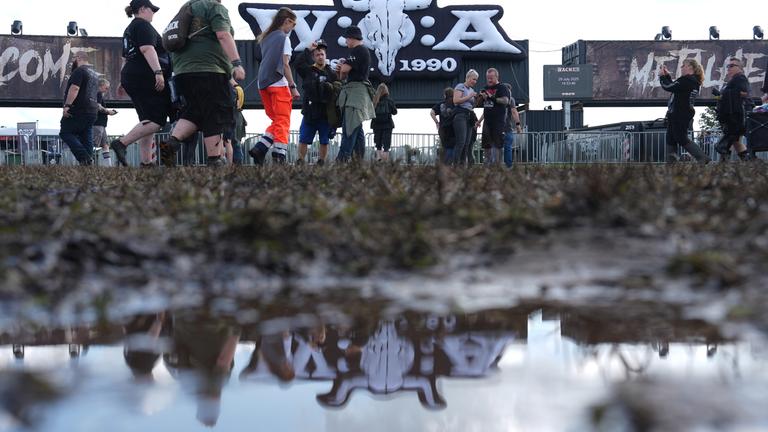 Metal-Fans gehen über das teilweise matschige Festivalgelände des Wacken Open Airs (WOA). 