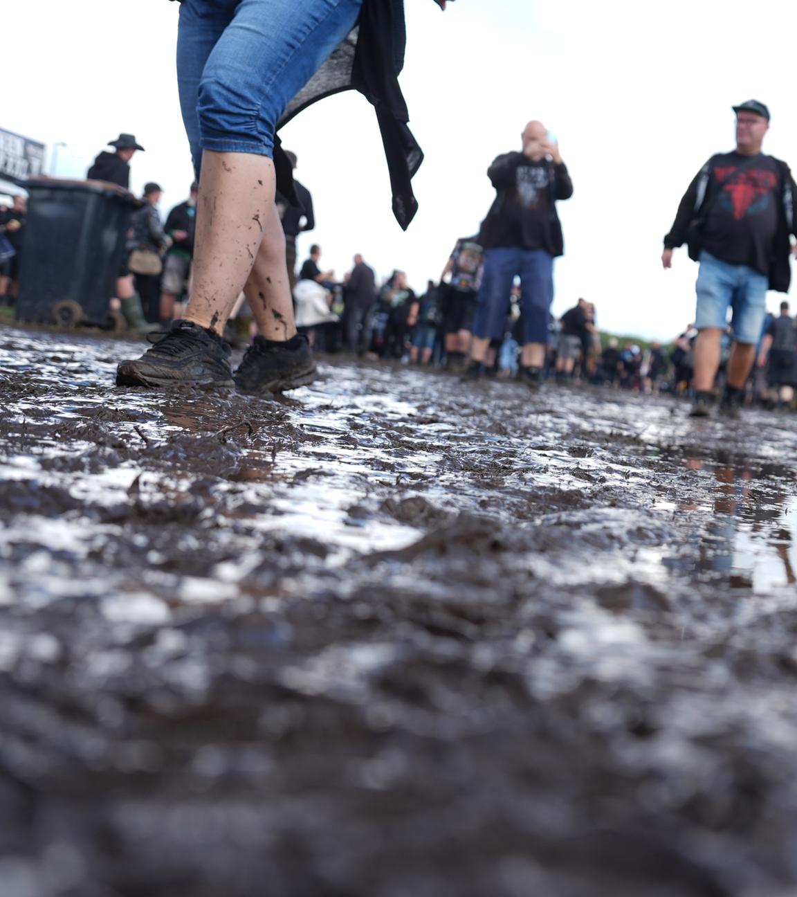  Metal-Fans gehen über das teilweise matschige Festivalgelände des Wacken Open Airs (WOA). 