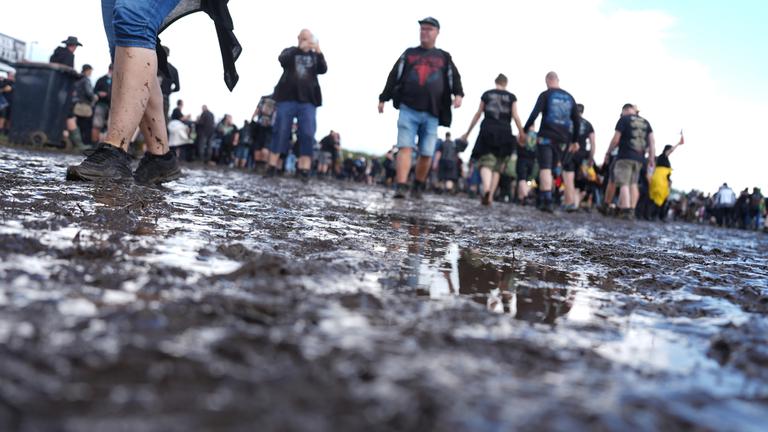  Metal-Fans gehen über das teilweise matschige Festivalgelände des Wacken Open Airs (WOA). 