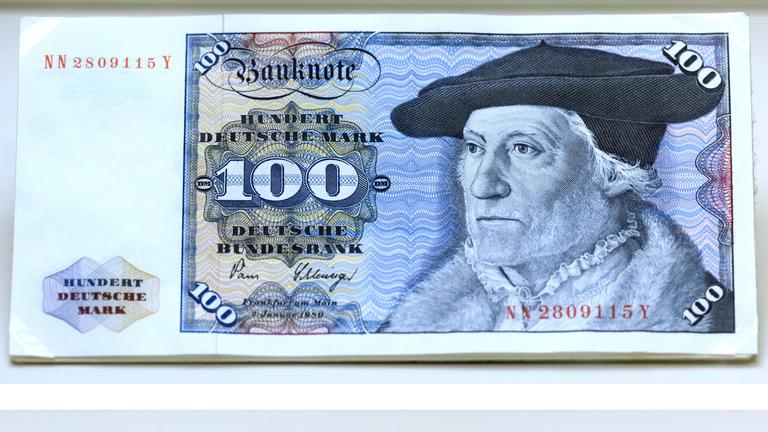 Eine 100 Mark Banknote der DDR und ein 100 D-Mark Schein der BRD. Beide sind blau.
