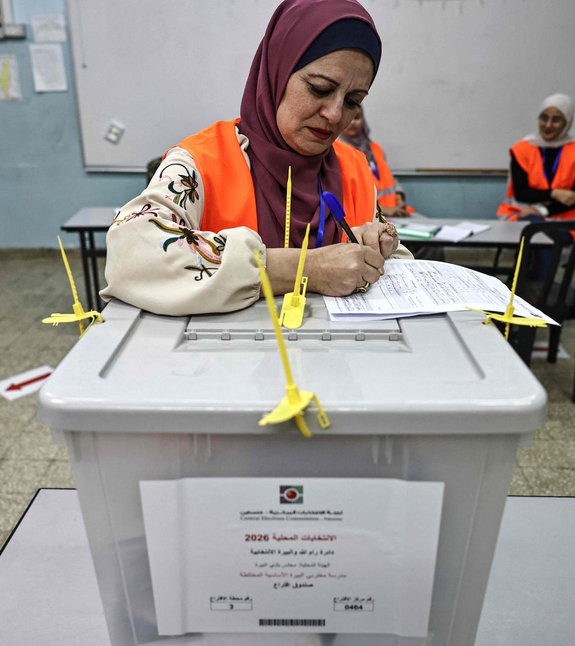 Eine Frau füllt einenZettel aus, der auf einer verschlossenen Wahl-Urne liegt.
