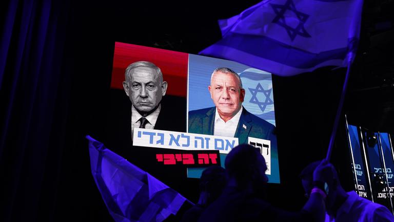 Bei einer Wahlkampfveranstaltung in der Dizengoff-Straße schwenken Menschen israelische Flaggen unter einem Transparent, auf dem Gadi Eisenkot (M) und der israelische Ministerpräsident Benjamin Netanjahu abgebildet sind. 