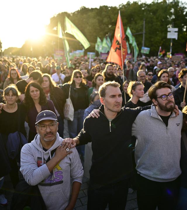 Menschen stehen mit Fahnen am Brandenburger Tor mit Blick auf die Siegessäule während einer Kundgebung. Unter dem Motto «Zeit zum Handeln: AfD stoppen!» hatten Campact und Fridays for Future zu der Kundgebung am Brandenburger Tor aufgerufen. Zu den angekündigten Rednern zählten die Berliner Linke-Spitzenkandidatin Eralp und der Linke-Bundesvorsitzende Pantisano.