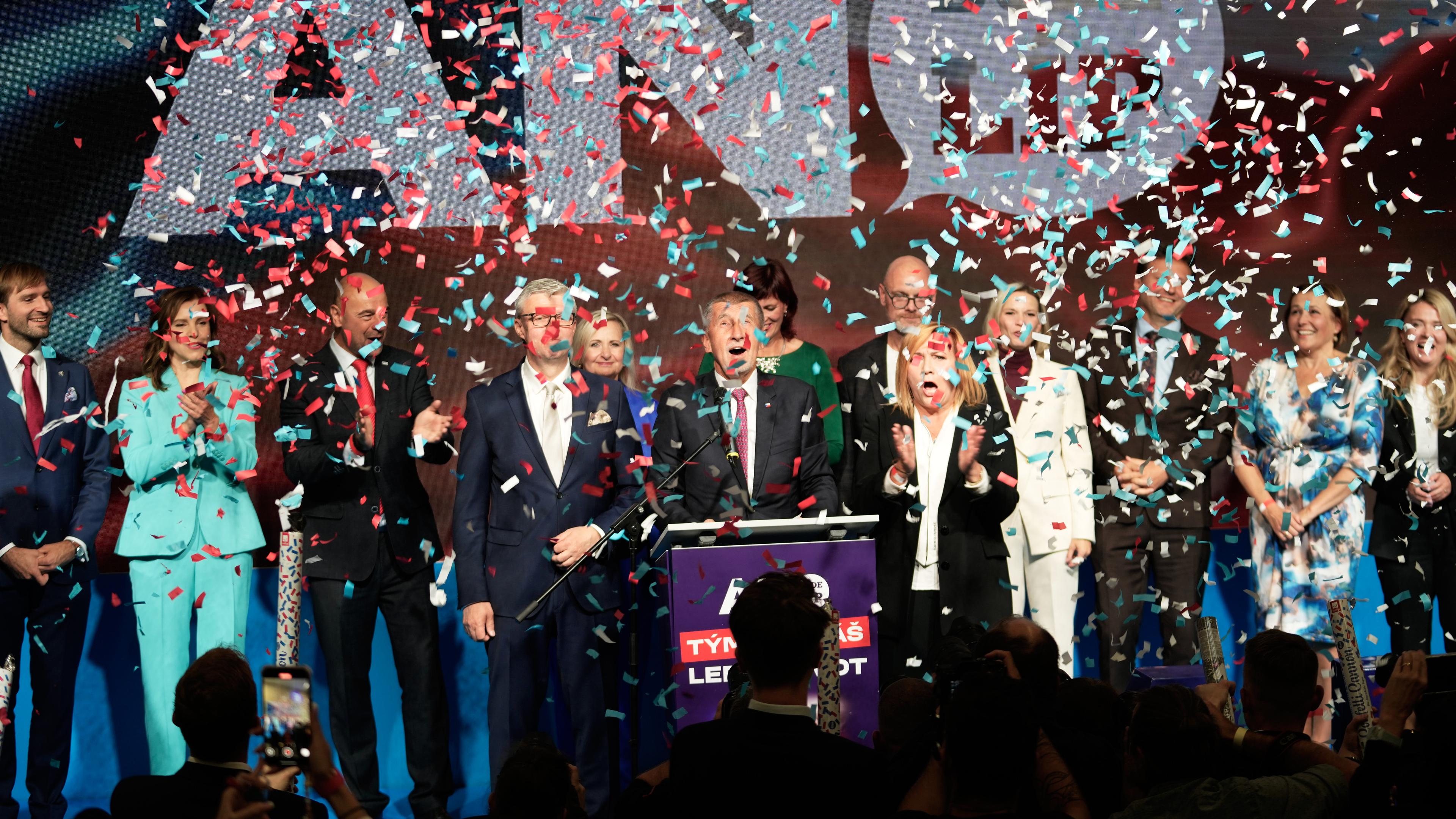 ANO-Parteispitze mit einigen Leuten um Andrej Babis auf einer Bühne, vor ihnen fliegt Konfetti.