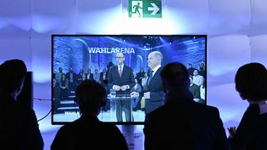 Die Kanzlerkandidaten Olaf Scholz (SPD) und Friedrich Merz sind auf einem Fernsehbildschirm im Studio der ARD-Wahlarena zu sehen.