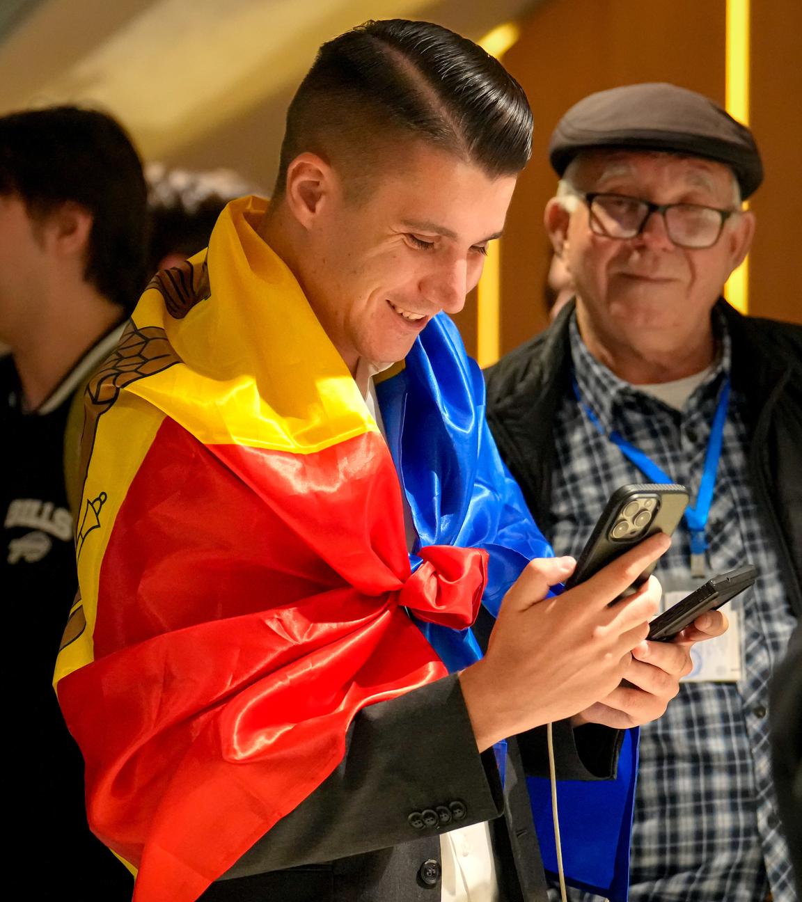 Ein Anhänger der pro-europäischen Partei „Aktion und Solidarität“ (PAS), der sich in die moldauische Flagge gehüllt hat, lächelt, während er nach Schließung der Wahllokale für die Parlamentswahlen am 28.09.2025, in Chisinau, Moldawien, die Teilergebnisse auf seinem Handy überprüft. 