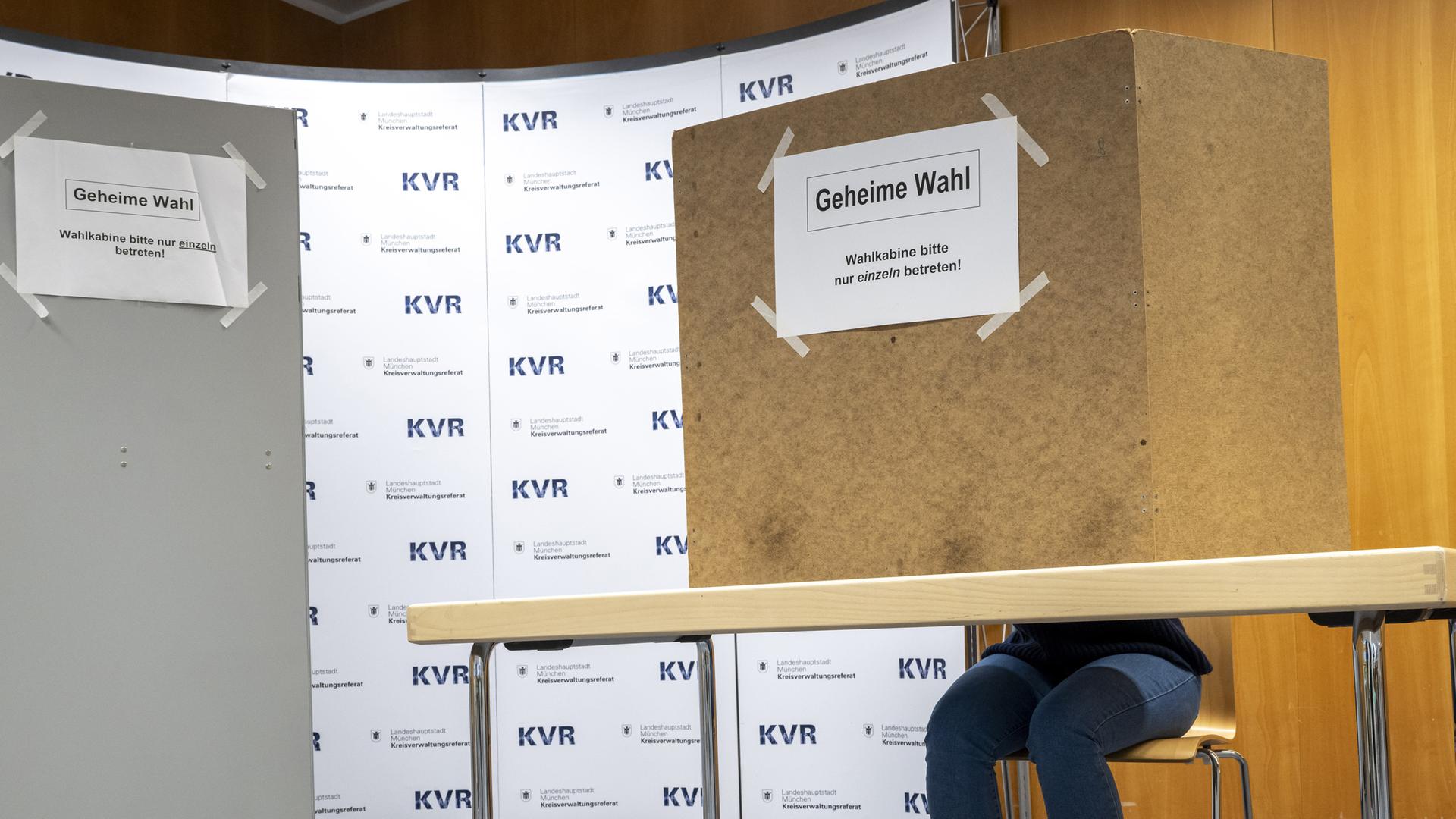 Eine Frau sitzt an einem Tisch mit einer Wahlkabine im Kreisverwaltungsreferat (KVR) der Landeshauptstadt München. 