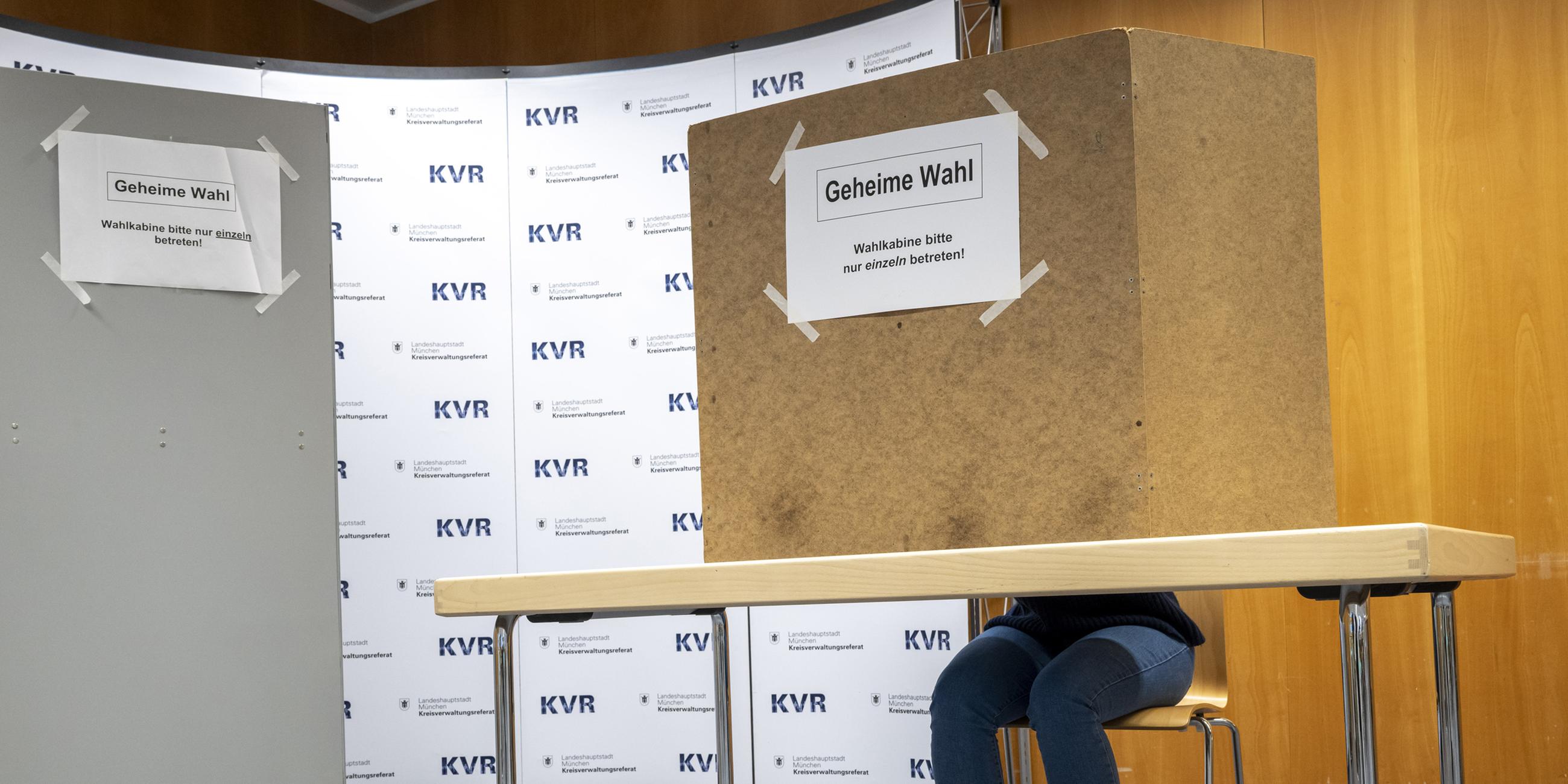 Eine Frau sitzt an einem Tisch mit einer Wahlkabine im Kreisverwaltungsreferat (KVR) der Landeshauptstadt München. 