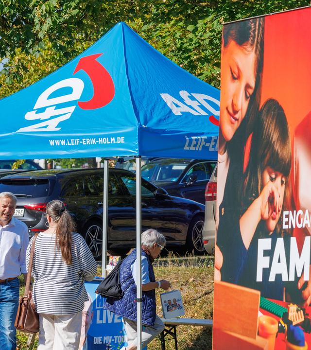 Leif-Erik Holm (2.v.l) , Ministerpräsidentenkandidat der AfD für die Landtagswahl in Mecklenburg-Vorpommern und Landesvorsitzender der Partei in Mecklenburg-Vorpommern, spricht an einem Informationsstand der Partei mit Passanten. Im Vordergrund ist ein Wahlplakat der SPD zu sehen