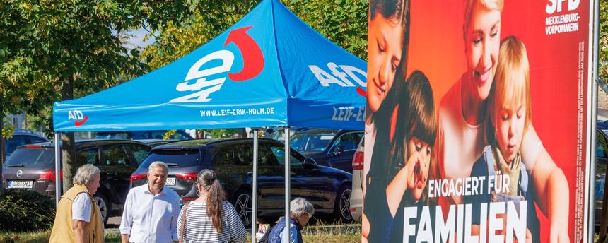 Leif-Erik Holm (2.v.l) , Ministerpräsidentenkandidat der AfD für die Landtagswahl in Mecklenburg-Vorpommern und Landesvorsitzender der Partei in Mecklenburg-Vorpommern, spricht an einem Informationsstand der Partei mit Passanten. Im Vordergrund ist ein Wahlplakat der SPD zu sehen
