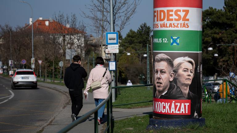 Menschen gehen an einem Wahlplakat mit der Aufschrift „Sie sind ein Risiko. Fidesz ist die sichere Wahl“ in Budapest vorbei, aufgenommen am Samstag, 14. März 2026, vor der Parlamentswahl am 12. April.