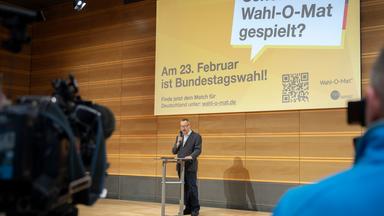 Ein Mann steht auf einer Bühne. Im Hintergrund ist eine Leinwand mit dem Hinweis auf den Wahl-O-Mat zu sehen.