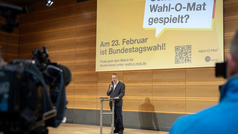 Ein Mann steht auf einer Bühne. Im Hintergrund ist eine Leinwand mit dem Hinweis auf den Wahl-O-Mat zu sehen.