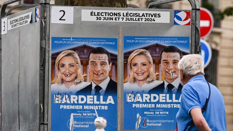 Ein Mann geht am 30. Juni an zerstörten französischen Parlamentswahlplakaten von Marine Le Pen, Präsidentin der Nationalen Rallye-Gruppe in der Nationalversammlung, und Jordan Bardella, Präsident der Nationalen Rallye, vorbei. 