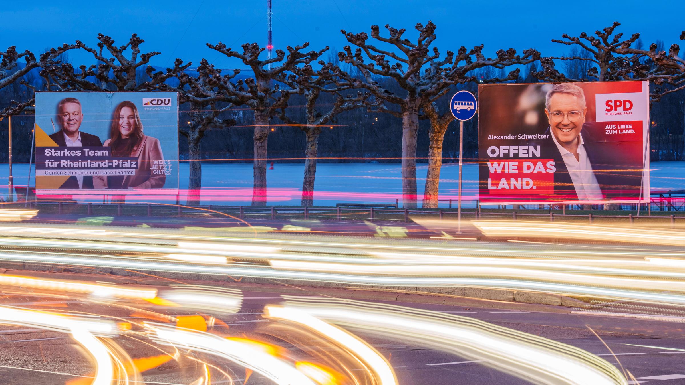23.02.2026, Rheinland-Pfalz, Mainz: Vorbeifahrende Fahrzeuge erzeugen auf der Rheinallee Lichtstreifen vor den Wahlplakaten von Gordon Schnieder (l-r, CDU), CDU-Landeschef und Spitzenkandidat seiner Partei, mit Isabell Rahms (CDU), Landtagskandidatin ihrer Partei für Mainz zur anstehenden Landtagswahl, und Alexander Schweitzer (SPD), Ministerpräsident von Rheinland-Pfalz und Spitzenkandidat der SPD. 