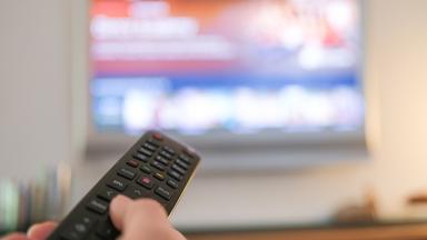 Personen richtet Fernbedienung auf Fernseher.