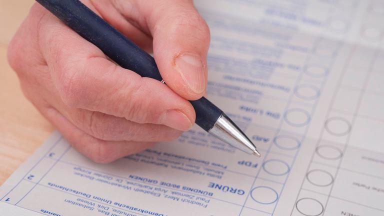 Eine Hand hält einen offenen Kugelschreiber über dem Stimmzettel zur Wahl des Bundestages.