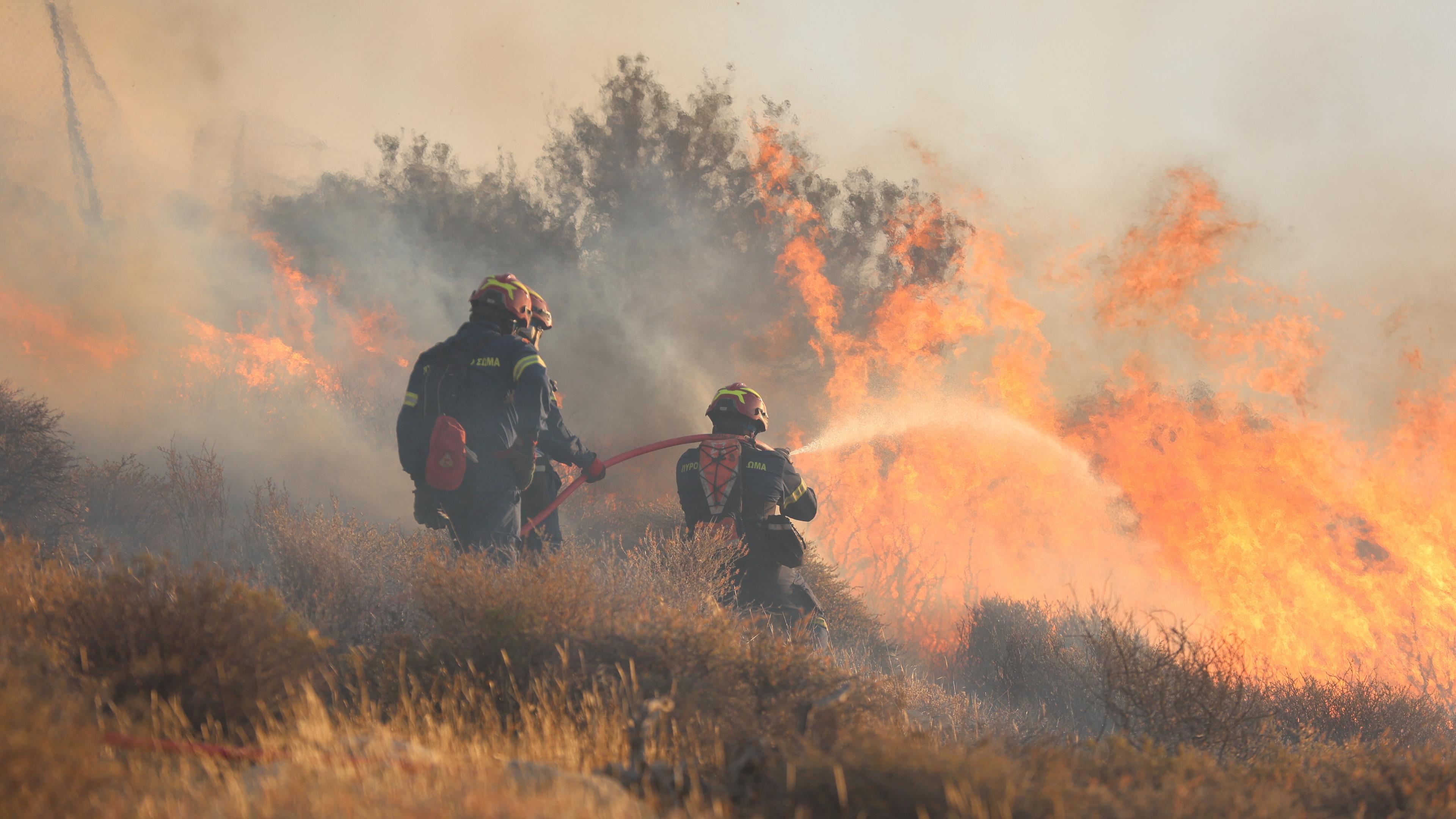 Feuerwehrmänner schießen Wasser mit Schlauch auf Brandherd.