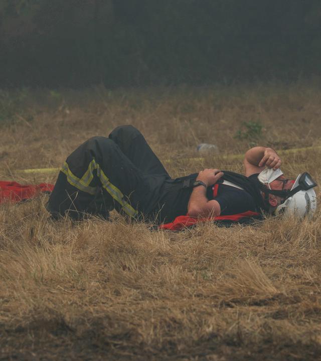 Ein Feuerwehrmann ruht sich am 29. Juli 2026 inmitten der Löscharbeiten bei einem Waldbrand nahe Lanton im Südwesten Frankreichs auf dem ausgetrockneten Gras aus. 