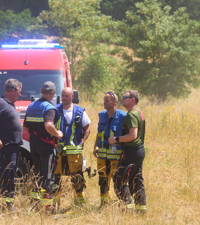 Feuerwehrleute und Waldbrand-Experten besprechen sich, während in der Nähe Rauch aus einem Naturschutzgebiet im Kreis Bad Kreuznach steigt. 