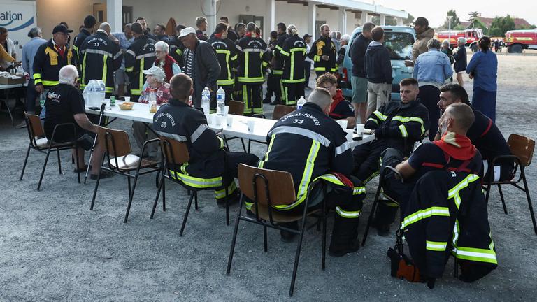 Feuerwehrleute und evakuierte Anwohner frühstücken vor der Gerard-Blanc-Festivalhalle in Le Porge im Südwesten Frankreichs. Nach dem Waldbrand wurden mehr als 2.000 Hektar zerstört.