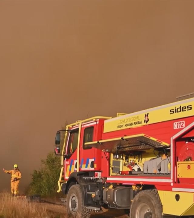 Ein Feuerwehrwagen vor dichtem Rauch im Wald.
