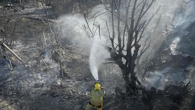Feuerwehrleute bewässern den Boden, nachdem sie ein Feuer gelöscht haben, bei dem ein Mensch ums Leben kam; der Brand ereignete sich am 25. Juli 2026 in einem Gebiet mit Gemüsegärten und Obstplantagen in einer Schlucht bei Manises im Osten Spaniens. 