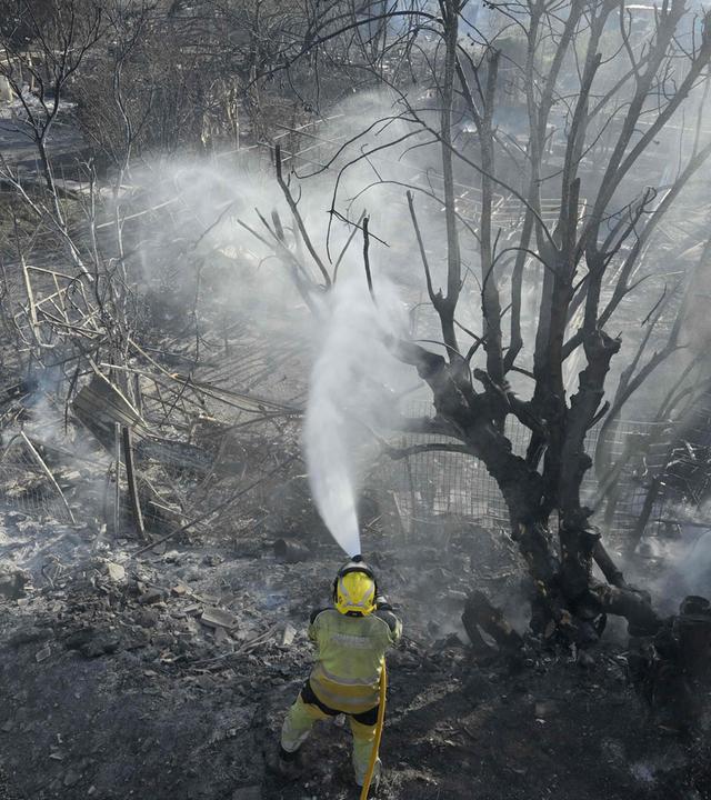 Feuerwehrleute bewässern den Boden, nachdem sie ein Feuer gelöscht haben, bei dem ein Mensch ums Leben kam; der Brand ereignete sich am 25. Juli 2026 in einem Gebiet mit Gemüsegärten und Obstplantagen in einer Schlucht bei Manises im Osten Spaniens. 