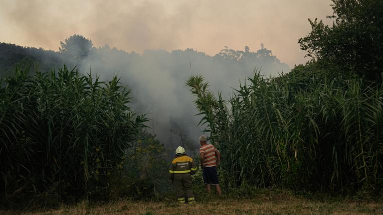 Zwei Personen beobachten das Feuer, das in der spanischen Provinz Galicien Häuser in den Dörfern O Pedreiro und O Urzal bedroht.