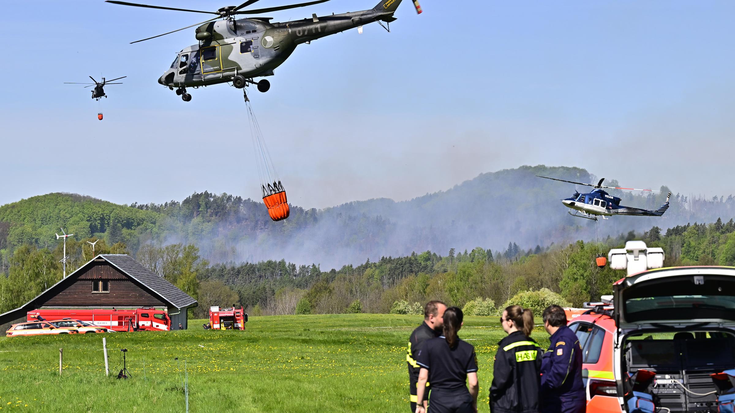 Hubschrauber fliegen mit Löschwasser-Behälter zu einem Waldbrand bei Rynartice im Nationalpark Böhmische Schweiz.