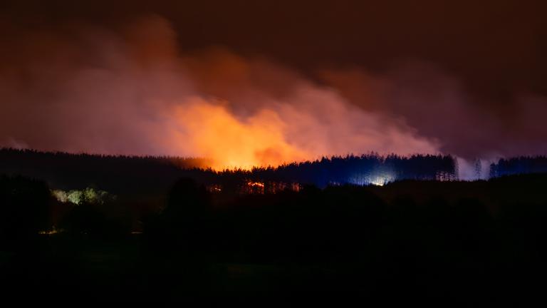 Ein Waldbrand erhellt den Himmel während Rauch aufsteigt.