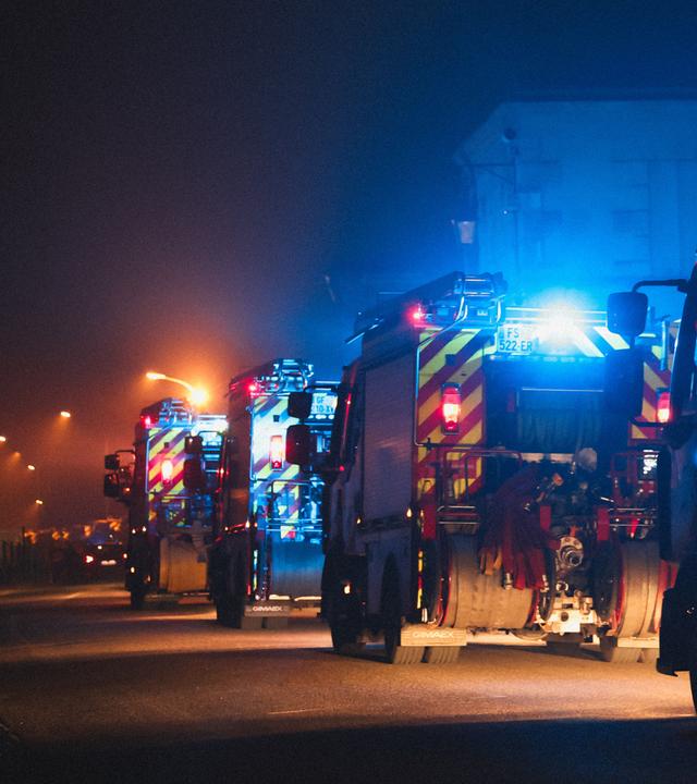 Eine Kolonne aus Feuerwehr-Wägen fährt hintereinander eine Straße entlang.