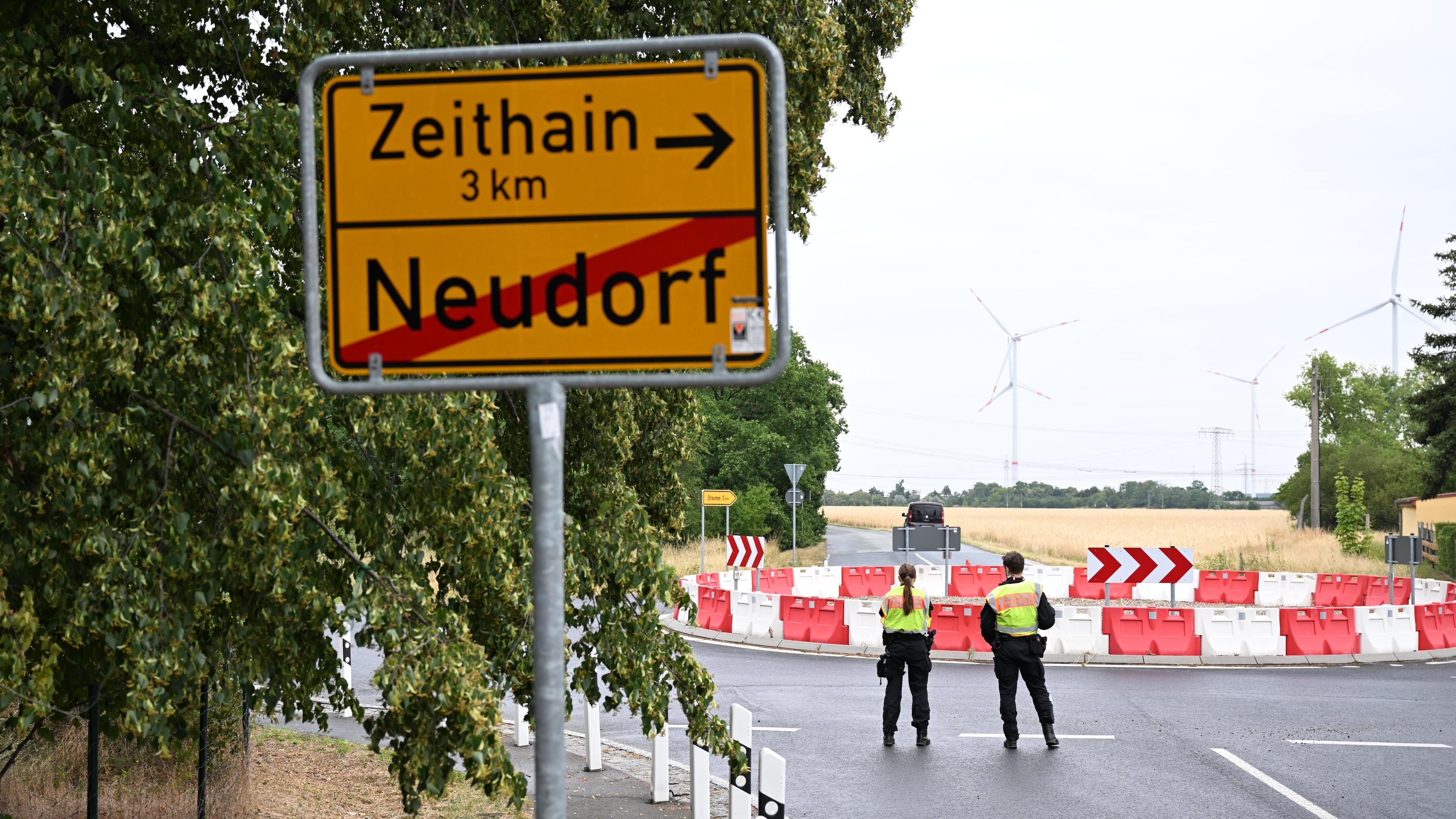 03.07.2025, Sachsen, Neudorf: Polizisten stehen anlässlich einer Evakuierung am Ortseingang hinter einer Ortstafel.