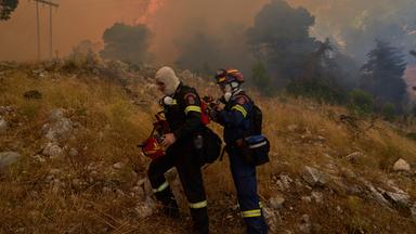 Zwei Feuerwehleute vor einem der Waldbrände in Griechenland.