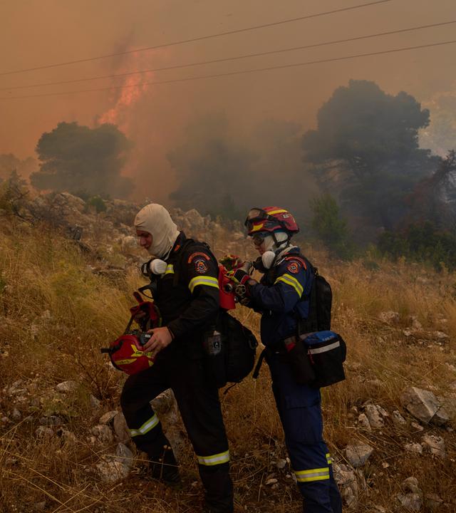 Zwei Feuerwehleute vor einem der Waldbrände in Griechenland.