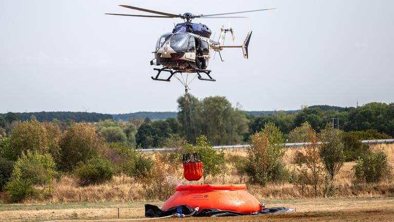 Ein Hubschrauber mit Wassersack nimmt nahe der Ortschaft Gey Löschwasser auf. Seit 15.08.2026