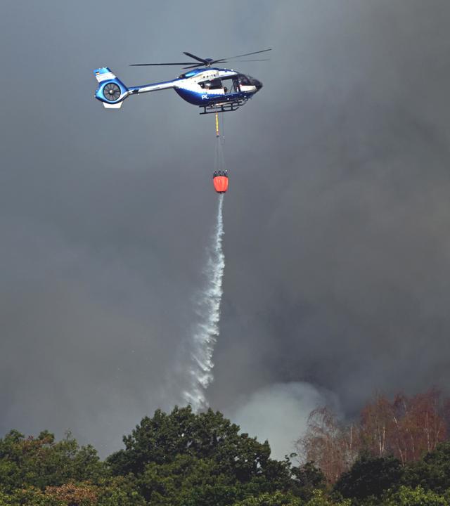  Ein Polizeihubschrauber mit Löschwasser-Außenlastbehälter unterstützt die Löscharbeiten beim Waldbrand im Hürtgenwald. 