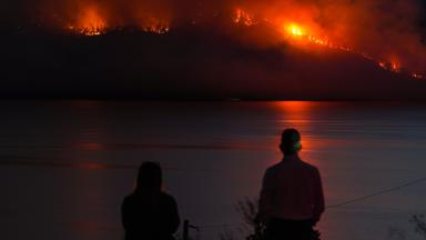 Einwohner beobachten, wie der Waldbrand am Quilpituk Creek am Berghang auf der gegenüberliegenden Seite des Okanagan-Sees in der Nähe von Fintry, British Columbia, wütet.