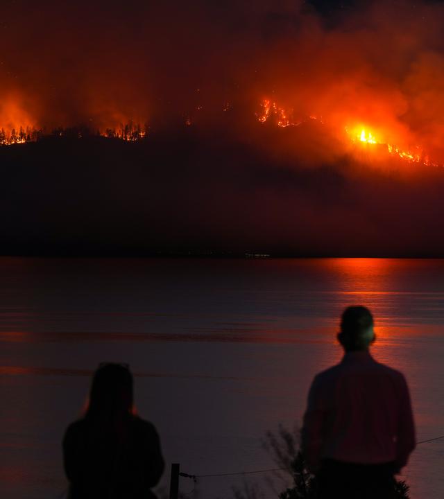 Einwohner beobachten, wie der Waldbrand am Quilpituk Creek am Berghang auf der gegenüberliegenden Seite des Okanagan-Sees in der Nähe von Fintry, British Columbia, wütet.