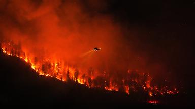 Ein Hubschrauber, der Nachteinsätze durchführt, bereitet sich darauf vor, Wasser auf den Waldbrand am Quilpituk Creek abzuwerfen, der auf der Westseite des Okanagan-Sees in der Nähe von Fintry (British Columbia) wütet.