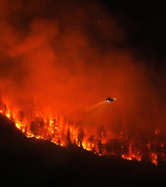 Ein Hubschrauber, der Nachteinsätze durchführt, bereitet sich darauf vor, Wasser auf den Waldbrand am Quilpituk Creek abzuwerfen, der auf der Westseite des Okanagan-Sees in der Nähe von Fintry (British Columbia) wütet.