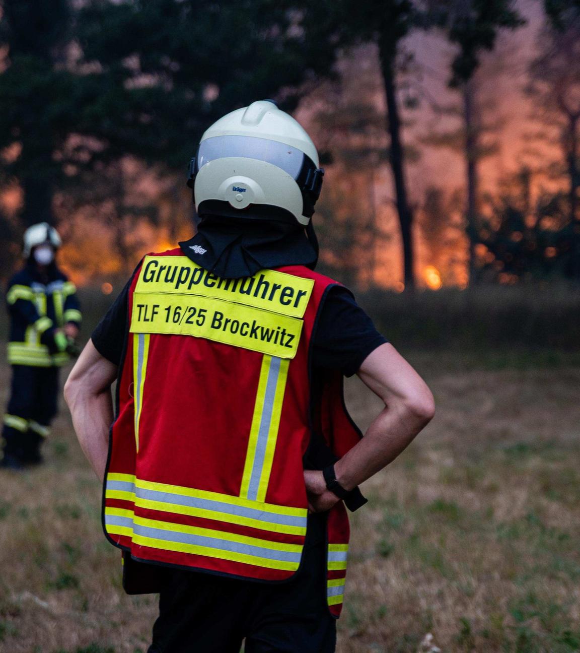 Ein Gruppenführer der Feuerwehr steht mit dem Rücken zur Kamera, den Blick auf einen Waldbrand gerichtet.