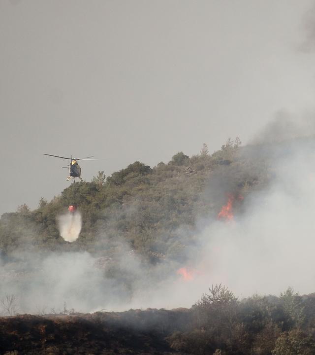 Ein Helikopter wirft über einem Brandgebiet Löschwasser ab.