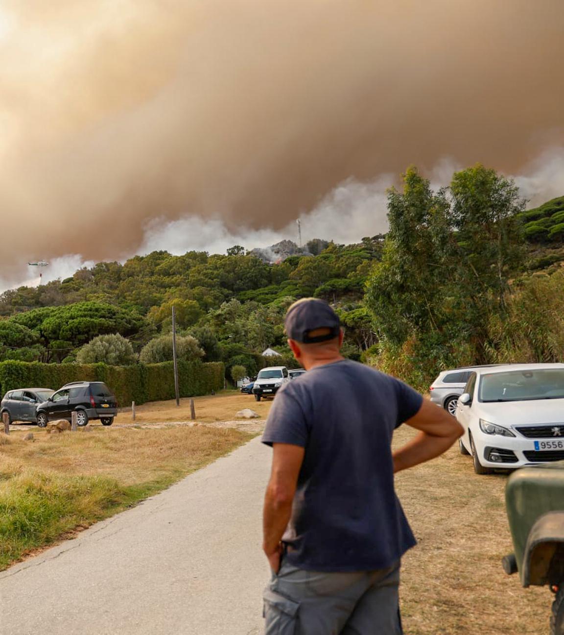 Aus dem Wald bei La Peña in Spanien, Cádiz steigt Rauch auf. Ein Gast des Campingplatzes Torre de la Peña in Tarifa steht an einer Straße und beobachtet das Geschehen. 