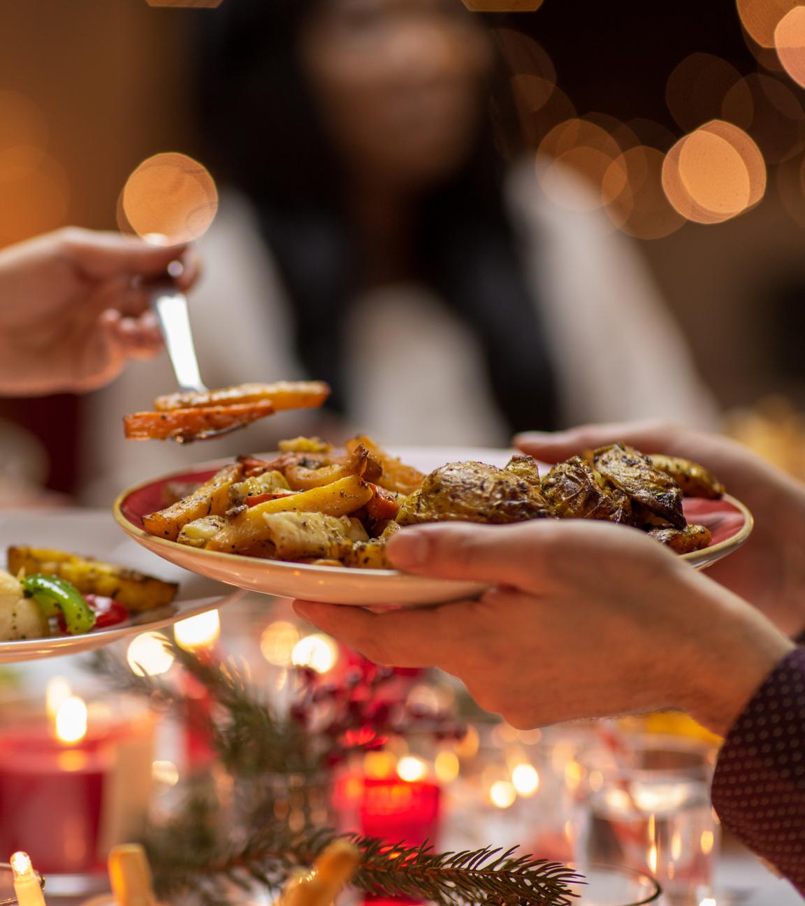 Menschen teilen gegenseitig Weihnachtsessen an einem gedeckten Tisch.