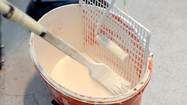 In einem Eimer voll Wandfarbe liegen ein Pinsel und ein Farbroller.