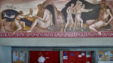 Ein Mann geht an einem Wandgemälde vorbei, das darstellt, wie Odysseus den Zyklopen Polyphem blendet. das Bild befindet sich an der Philosophischen Fakultät der Nationalen und Kapodistrias-Universität Athen
