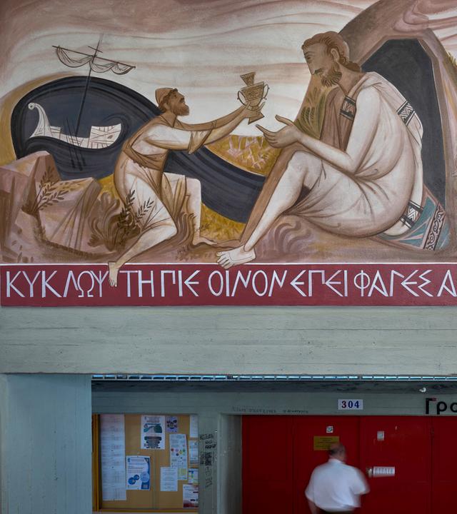 Ein Mann geht an einem Wandgemälde vorbei, das darstellt, wie Odysseus den Zyklopen Polyphem blendet. das Bild befindet sich an der Philosophischen Fakultät der Nationalen und Kapodistrias-Universität Athen