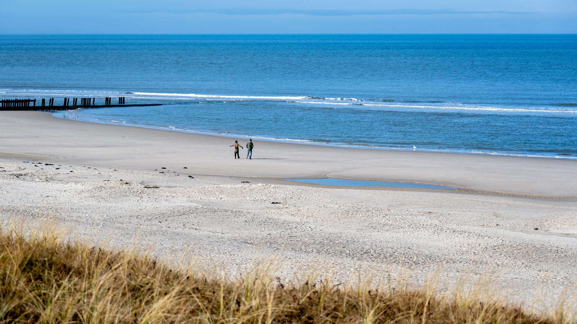 Niedersachsen, Wangerooge: Spaziergänger sind bei sonnigem Wetter am Strand der Insel unterwegs
