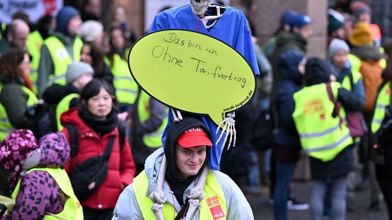  Beschäftigte der Uniklinik Köln halten bei einen Warnstreik vor dem Haupteingang ein Skelett hoch